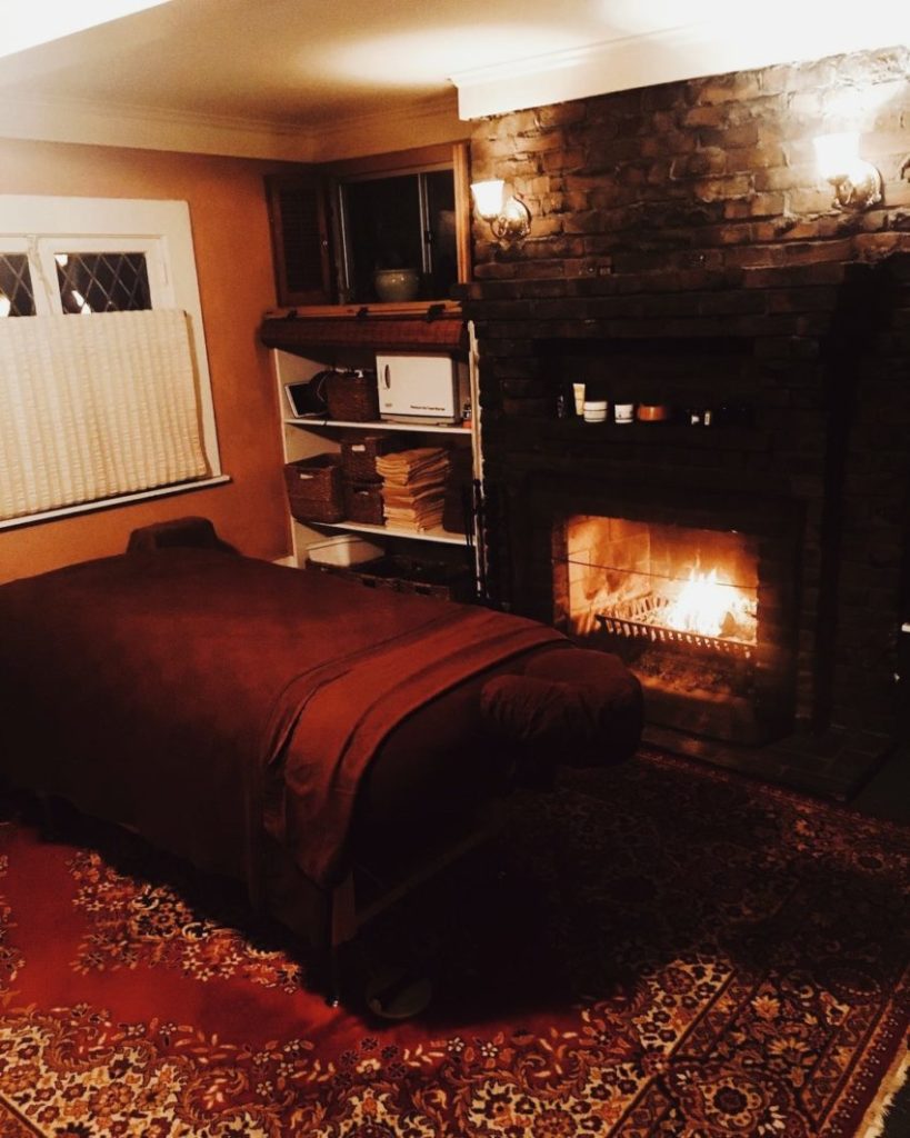 Warm fireplace illuminating massage table. Eed persian rug and res sheets on the massage table.